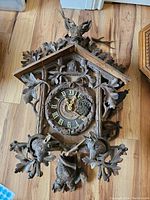 Front view of carved Black Forest cuckoo clock case with dial, stag head, deer heads and oak leaf carvings attached with detached pieces laid around