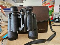 Front view of vintage Bushnell Sportview 10x50 binoculars with leather carry case visible behind.