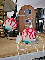 Two eyeball-shaped glass lamp shades with red vein designs and blue irises attached to flexible metal gooseneck arms and a silver metal base, with cord and plug visible.