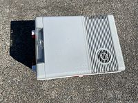 Closed top view of the white plastic electric cooler with ventilation grill and red handles.