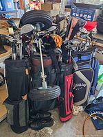 Front view of lot showing multiple golf bags filled with assorted clubs, push cart wheels at front, golf shoes at base