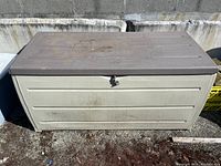 Photo of large beige plastic tote with brown hinged lid and latch on front showing dirt and wear from outdoor use