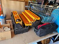 Black plastic tackle box open displaying yellow trays and items inside, placed on a table next to a black soft bag.