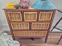 Front view of wooden storage unit with six woven drawers and items on top.