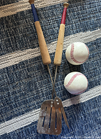 Photo showing the baseball-themed BBQ set including the spatula, fork, and two baseball salt and pepper shakers on a blue and white striped rug.
