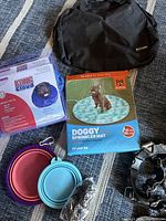 Photo showing boxed Kong Cloud protective collar, Fidos Doggy Sprinkler box, two collapsible bowls in blue and pink, and black carrying bag.