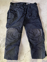 Front view of black First Gear motorcycle pants displaying reinforced knee areas and lower leg zippers.