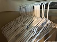 Photo showing a set of white plastic hangers hanging closely together on a rod