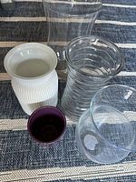Top view capturing all five vases showing variety in clear glass and ceramic shapes and textures on striped cloth background.