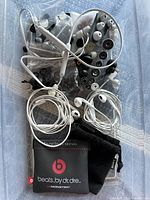 Top view of various earbuds and accessories in plastic bag showing Apple style earbuds, Beats branded pouch and multiple ear tips.