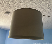 White cylindrical lamp shade hanging from ceiling, smooth fabric surface, 17 inches diameter.