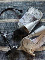 Three silver-colored IKEA lighting items on a textured surface: one clamp-on flexible desk lamp and two hanging fixtures, all new and wrapped in original plastic packaging with IKEA tags.