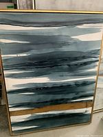 First abstract framed print showing horizontal blue and white striped pattern with gold accent and thin gold frame.