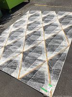 Photo showing the full view of the rectangular area rug laid flat on asphalt surface, highlighting its geometric pattern in grays and beige.
