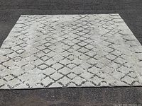 Top-down view of full 10'x8' off-white area rug with grey diamond pattern on asphalt surface