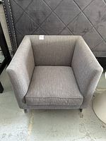 Front view of gray upholstered armchair with seat cushion and square armrests.