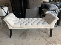 Front angled view of the white upholstered bench showing tufted fabric and wood legs.