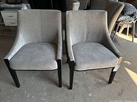 Front view of both chairs showing light grey fabric upholstery on seats and backs and black wooden legs.