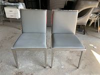 Front view of two modern chairs with metal frames and gray faux leather upholstery.