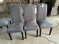 Three grey upholstered dining chairs with metal stud details and dark wood legs, placed side by side.