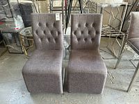 Front view of the two brown upholstered dining chairs with tufted backs in a warehouse setting.
