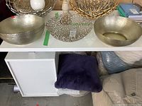 Four decorative metal bowls displayed on white shelf, two hammered metal silver colored bowls and two openwork patterned bowls.