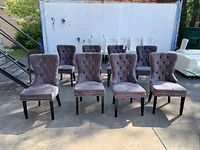 Eight gray tufted dining chairs arranged outdoors against white container