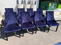 Eight navy velvet tufted dining chairs arranged outdoors next to white chairs and a dumpster