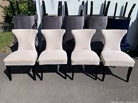 Front view of four beige upholstered dining chairs with black legs arranged in a line outdoors.