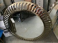 Full front view of the round mirror showing metal frame with decorative wave cut-outs and visible gap between mirror surface and frame.