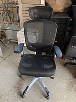 Front angled view showing the black mesh seat, plastic base, caster wheels, and armrests of the office chair.