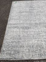 Overview of the light gray ornate patterned area rug laid flat, showing the decorative pattern and some staining.