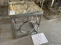 Side table front view showing mirror top and geometric chrome base pattern with a circle element in the center.