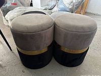 Two round storage ottomans in light gray microfibre with black base and gold metal band, showing overall appearance and condition.