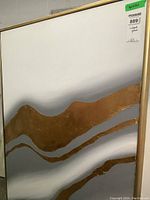 Frontal view of large abstract textured canvas print with wavy gold and gray tones and light wood frame, showing signs of wear and sticker label on top right.