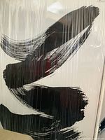 Front view of the framed textured abstract print wrapped in plastic showing black brushstroke design on white canvas.
