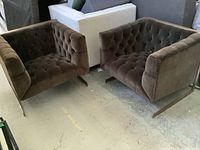 Pair of two brown velvet tufted tub chairs side by side on concrete floor