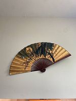 Large Asian decorative wall fan mounted on white wall showing the floral and bird painting, wooden ribs with reddish-brown finish.