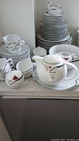 Overview of stacked plates, bowls, cups, teapot, sugar bowl, creamer and platter.