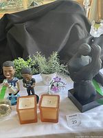 Shot showing kissing couple black sculpture, two Toronto Argonauts bobbleheads, two faux succulent plants in square containers, and two candles.