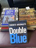Photo showing five books stacked on a table, titles visible including history, cooking, and sports.
