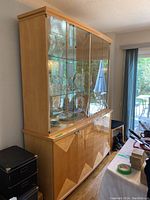 Full view of the china cabinet showing the light wood finish, glass hutch, and the angular geometric door details on the lower cabinet.