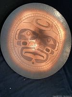 Front view of a circular copper plate featuring a detailed etched Moon face design characteristic of Northwest Coast Indigenous art.