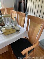 Photo showing six wooden dining chairs lined up at a table with black upholstered seats and light wood frames.
