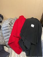Three outerwear pieces: two wool blend capes (black and red) and one silver quilted puffer jacket, all size medium.