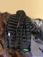 Front view of black mixed material jacket with textured horizontal stripes and collar.