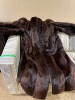 Full view of the brown muskrat fur jacket laid out on a couch showing front exterior and sleeves.