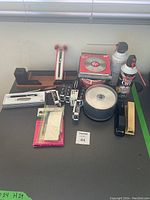 Wide shot showing all office supplies including pens, CDs, Dust-Off cans, envelope openers, and stapler on a black surface.