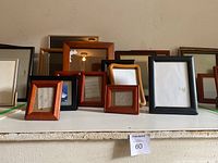 Photo showing assortment of picture frames in various sizes and finishes arranged on a white shelf.