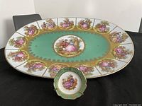 Large platter with central scene and smaller surrounding romantic vignettes on green background and gold trim, with small matching plate in front.